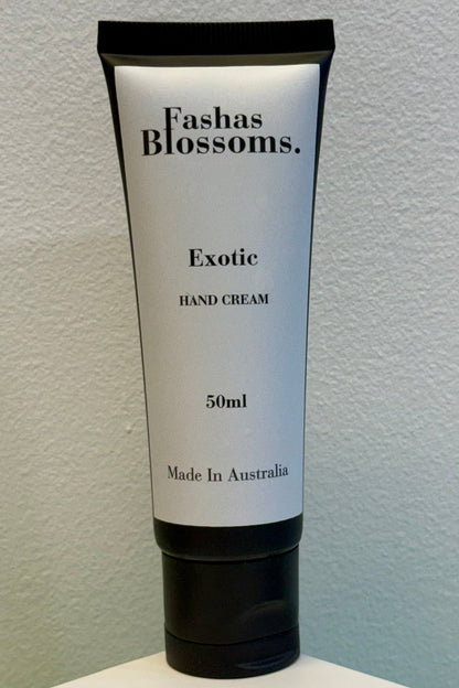 A 50ml squeeze tube of Fashas Blossoms Exotic Hand Cream, featuring a white label with black text and a black cap, standing on a white surface against a light blue-gray textured wall.