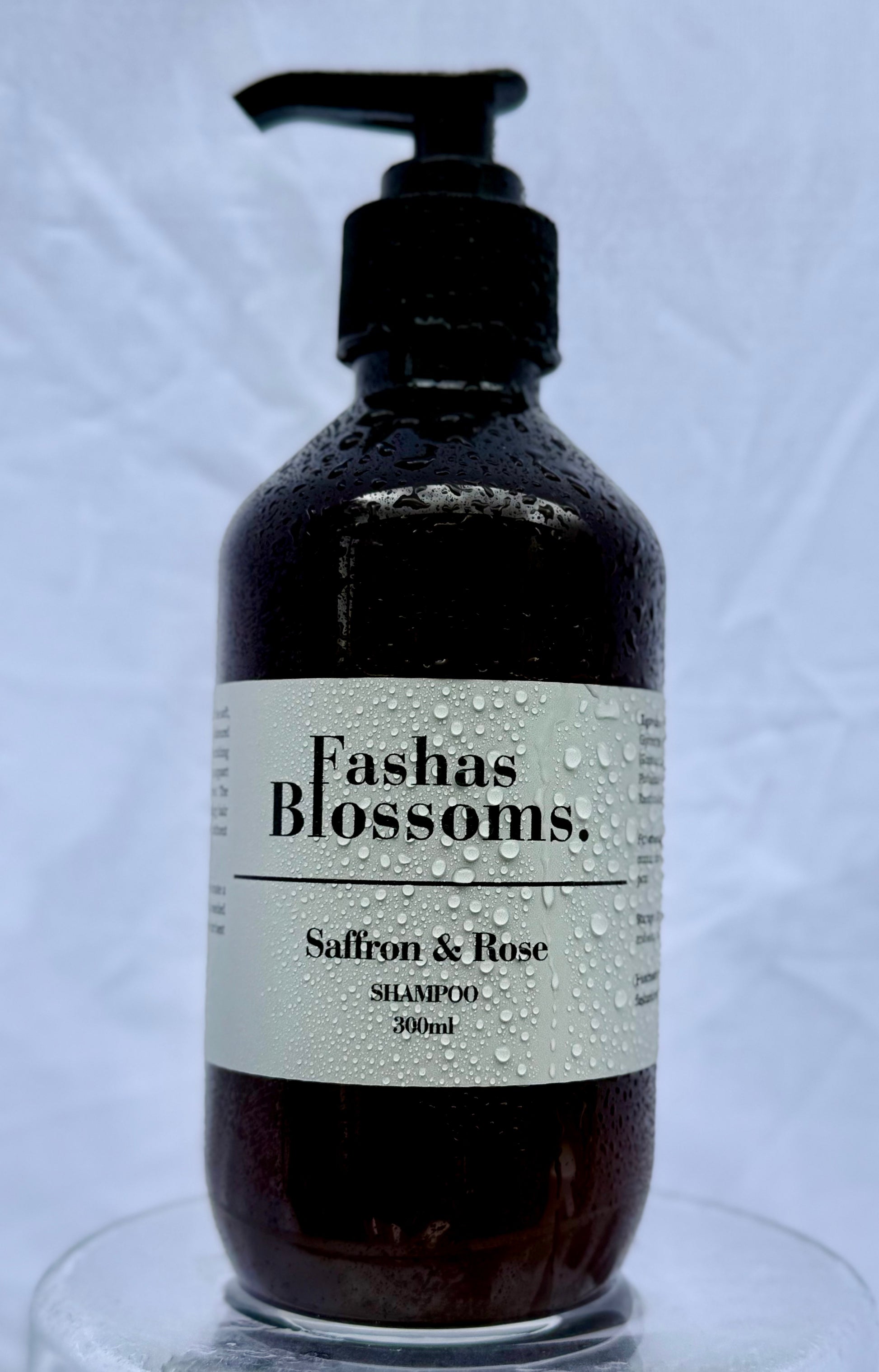 Bottle of Fashas Blossoms Saffron & Rose shampoo on a clear stand with a light gray background