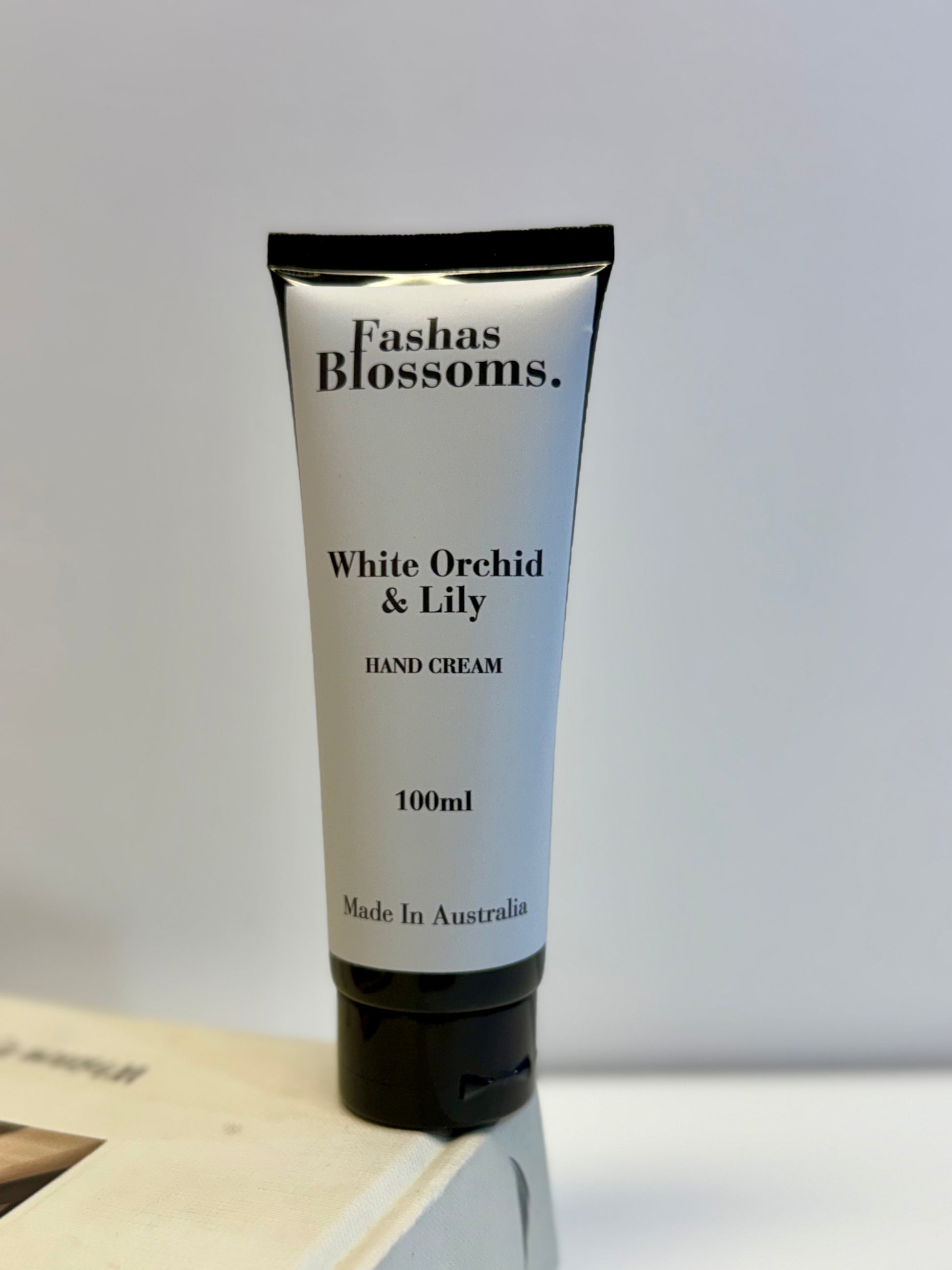 Hand cream tube labeled 'Fashas Blossoms White Orchid & Lily' on a light gray background