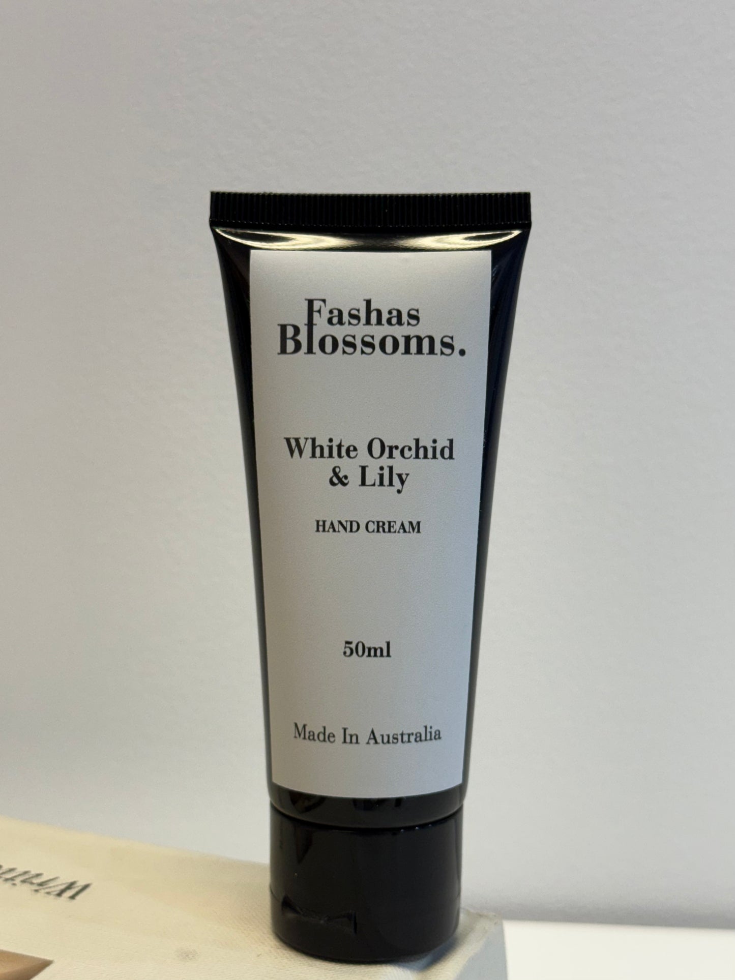 Hand cream tube labeled 'Fashas Blossoms White Orchid & Lily' on a light gray background